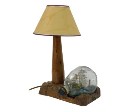 A 20thC oak desk lamp, modelled as a light house with shade, on a carved base, together with a ship in glass bottle titled Th