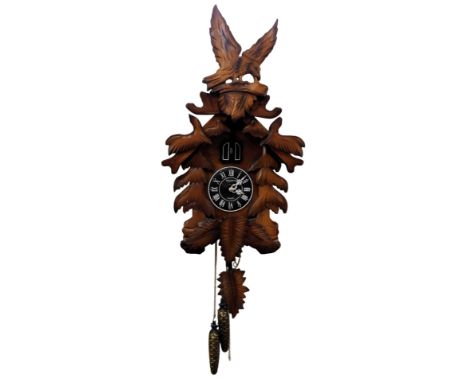 A 20thC cuckoo clock, with circular dial bearing Roman numerals, quartz movement, in an elaborate leaf carved case surmounted