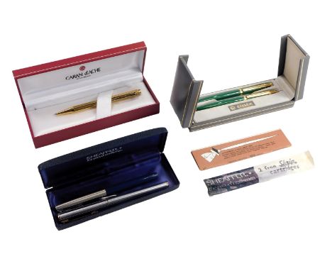 A Caran d'Ache ball point pen, in gold coloured engine turned decoration, together with an Elysee two pen set, in green, and 