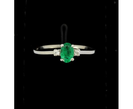 A 9ct white gold ring set with an oval cut emerald and diamonds, needs re-straightening, (T.5).