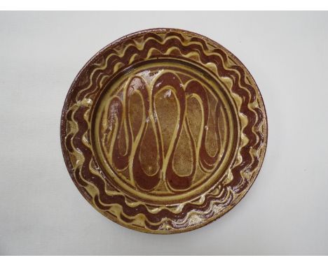 An early Winchcombe Pottery slip ware dish with finger wipe waved deatil. Impressed seal. 24cm diameter