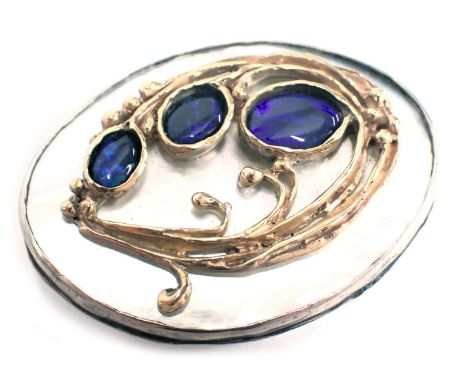 A Danish Art Nouveau oval brooch, with rub over border on mother of pearl backing shell, set with three fire opals, with leaf