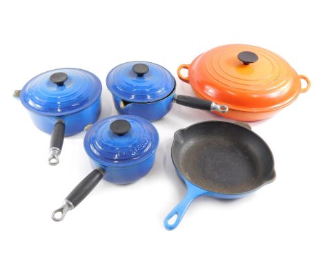A large orange enamel Le Creuset circular pan, and other blue enamel Le Creuset pans. 