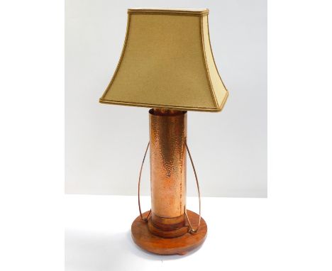 An Arts and Crafts type copper and oak table lamp, of twin handled hammered form, raised on a stepped circular base, with sha