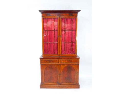 A Victorian flame mahogany cupboard bookcase, the outside pediment over two glazed doors, opening to reveal three height adju