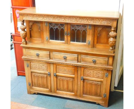 An Elizabethan style oak court cupboard, with carved S scroll top frieze, raised on leaf carved cup and cover turned supports