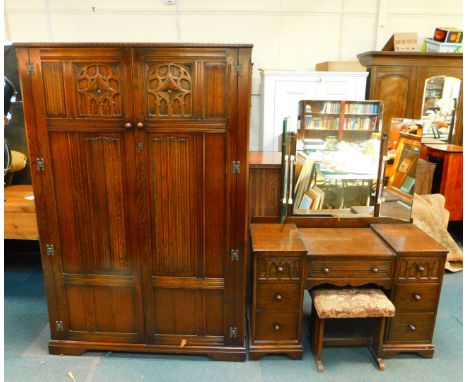 A Tudor style oak double wardrobe, with linenfold and Gothic arch tracery panelled doors, opening to reveal a shelf above han