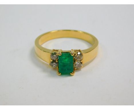 An emerald ring, flanked by two pairs of diamonds in a stepped shank, yellow metal stamped 18K, emerald approximately 1/2 car