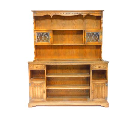 An Old Charm style oak dresser, the outswept pediment over a two shelf plate rack, with glazed cupboards, over three central 