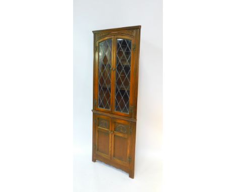 An Old Charm oak corner cabinet, the slightly outswept pediment over two glazed doors opening to reveal to shaped shelves, ab