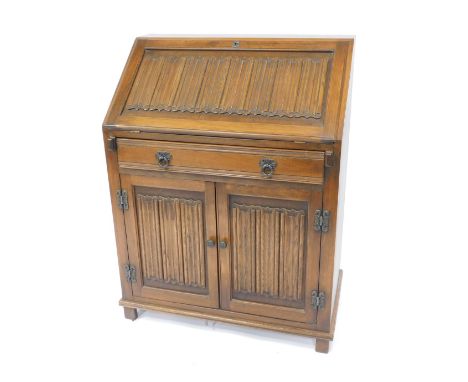 An Old Charm oak bureau, with linen fold panel to the fall front, with shallow drawer below, and cupboard enclosed by two lin