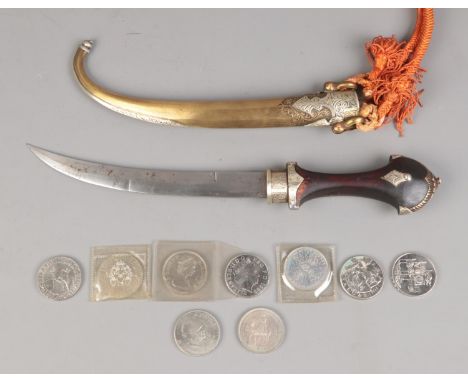 A Morroccan Jimbaya dagger featuring brass and white metal scabbard along with small quantity of British commemorative crowns