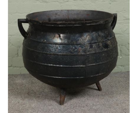 A large twin handled cast iron cauldron planter. Height: 50cm, Diameter: 52cm.  Rust hole to the base, one leg detached.