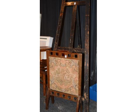 A vintage folding wood picture easel, 181cm high, together with Arts & Crafts style oak firescreen with embroidered tapestry,