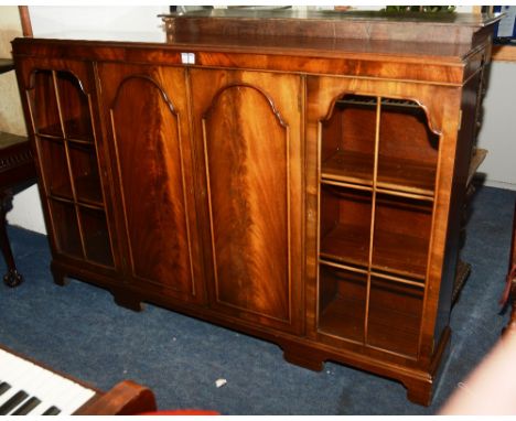 A mahogany bookcase, with two panelled doors flanked by a glazed door enclosing shelved interior, raised on bracket supports,