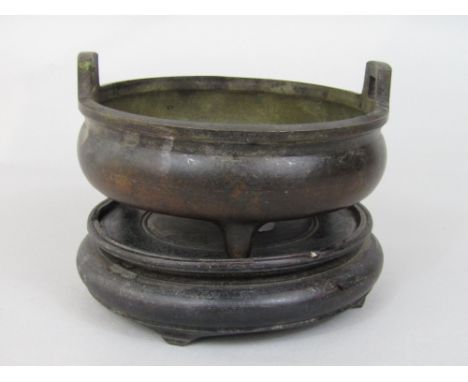 Antique Chinese cast bronze twin handled sensor upon three feet, calligraphy mark to base, 15cm diameter upon a hardwood stan