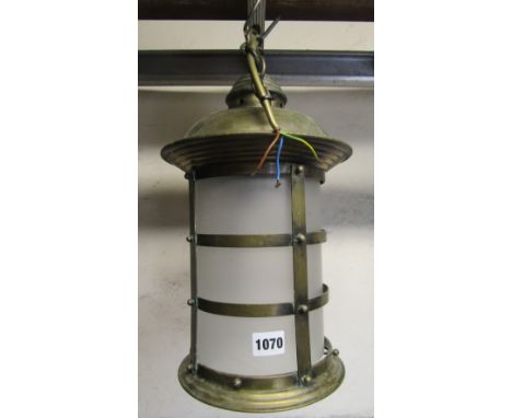 A brass hall/porch lantern of cylindrical form with strap work frame and frosted shade