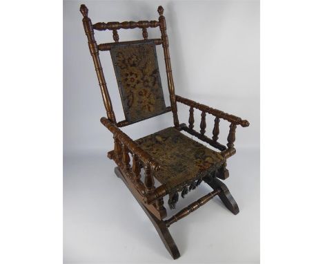 An Antique Child's Rocking Chair. The chair having turned back and arm supports, on bracket base, original tapestry seat and 