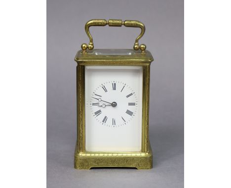 A brass carriage timepiece with all-over engraved scroll decoration, the white enamel dial with black roman numerals, 12cm.