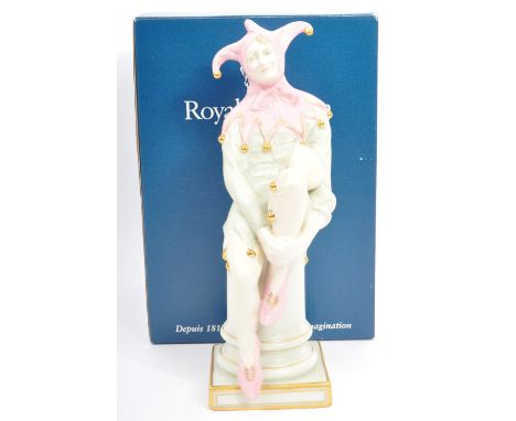 A Royal Doulton table top porcelain china figurine of 'The Jester'. HN3922. In a seated position on a pedestal in light paste