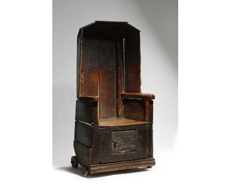 A WELSH PRIMITIVE ELM LAMBING / COMMODE CHAIR 17TH / 18TH CENTURY AND LATER the hooded top above a boarded seat with a circul