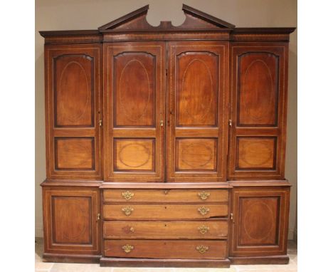 A George III mahogany breakfront linen press or housekeepers cupboard, outlined and detailed with serrated and checkered band