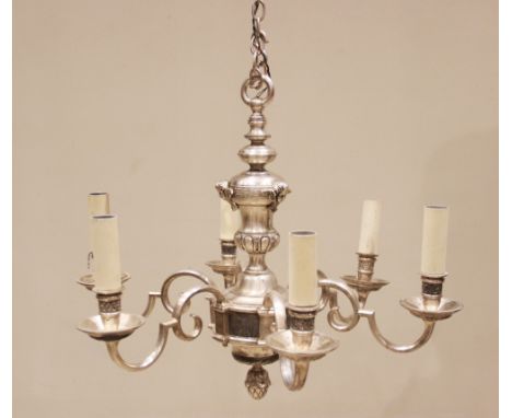 A white metal six branch chandelier, the urn shaped column applied with cast cherub masks, extending to six scrolled arms abo