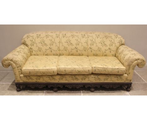 A Victorian carved oak sofa, later re-upholstered in foliate fabric, the scalloped padded back rest extending to scrolled arm