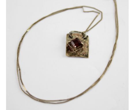 A 9ct gold fine link chain marked '375' to the clasp with yellow metal hand-beaten pendant with central red paste stone, appr