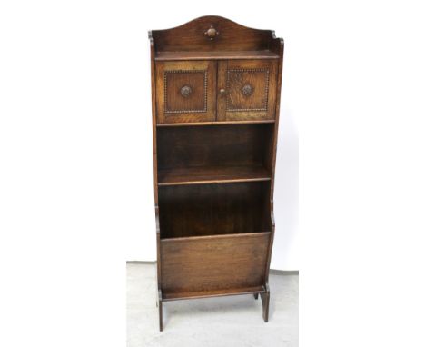 A c1930s oak slender bookcase, two small cupboard doors over one shelf and lower magazine rack, to block supports, 124 x 45cm