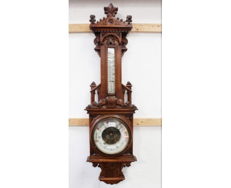 A late 19th/early 20th century oak barometer, floral carved pediment over Fahrenheit and centigrade thermometer over ceramic 