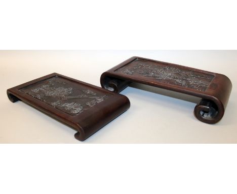 TWO SIMILAR CHINESE WOOD STANDS, with scroll ends, each top surface decorated in relief with a river landscape scene, the lar