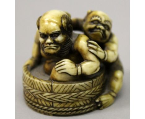 A JAPANESE STAINED IVORY NETSUKE OF TWO ONI, one of whom washes the back of his companion who sits in a wood grained circular