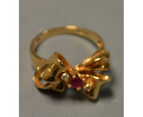 A ruby and diamond ring, tied ribbon bow setting set with a central single round pinky red ruby, flanked by two diamond accen