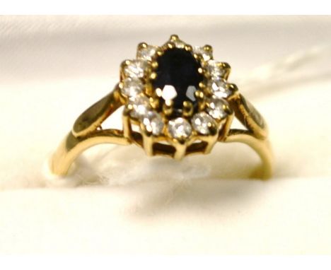 A 9ct gold diamond and sapphire flower head cluster ring, central oval deep blue sapphire, surrounded by a band of twelve rou