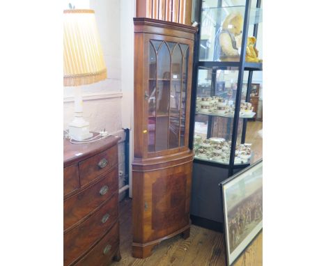 A crossbanded walnut corner cabinet, with glazed door over a bowed cupboard door on bracket feet, 64cm wide, 181cm high