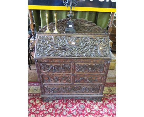 An Anglo-Indian hardwood bureau, profusely and deeply carved with flowers and foliage, the sloping fall enclosing a fitted in