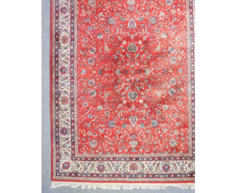 An Eastern carpet of "Persian" design woven in colours with bold trailing floral ornament, on a terracotta ground, within con