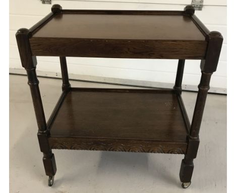A vintage dark oak 2 tier tea trolley on wheels with carved detail to front.  Approx. 71cm tall x 64.5cm wide.