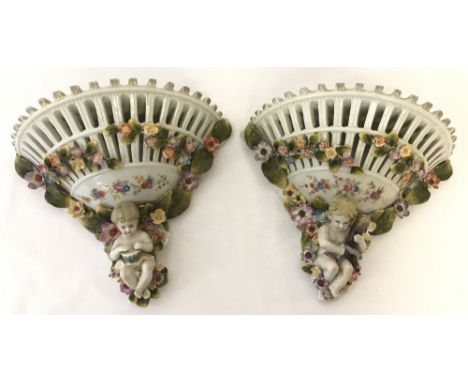 A pair of ornamental ceramic wall hanging shelves decorated with flowers and cherubs. With pierced work detail. Reverse shows