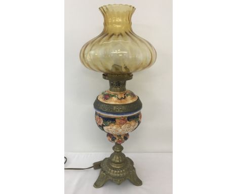 A vintage ceramic and brass lamp base with amber glass shade. Lamp bowl has cherub panel detail and heavy brass base on tripo