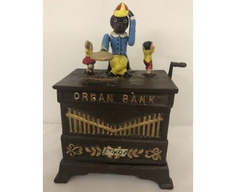 A wind up cast iron money box of an organ with monkey. With painted detail. When wound the monkey drops the coin from his tra