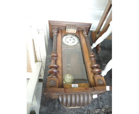 An antique wall mounted clock with visible mechanism and enamel face 