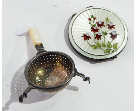 A compact of circular form with enamelled decoration, decorated with fuschias and a silver tea strainer with mother-of-pearl 