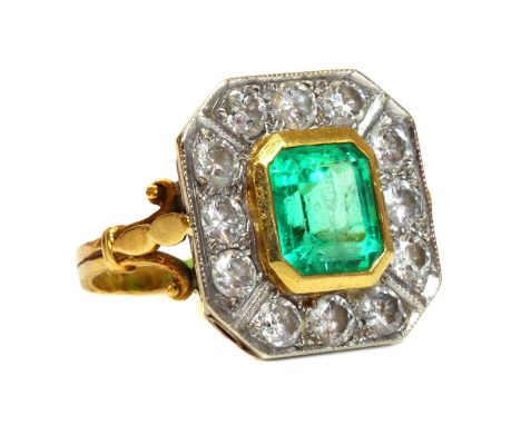 An 18ct gold emerald and diamond octagonal cluster ring,with an emerald cut emerald, rub set in yellow to the centre. A borde