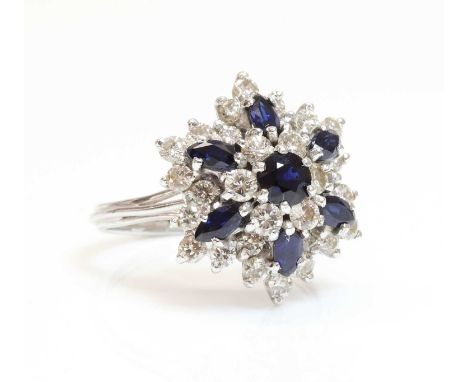 A white gold sapphire and diamond snowflake cluster ring,with a central circular mixed cut sapphire, surrounded by a row of b