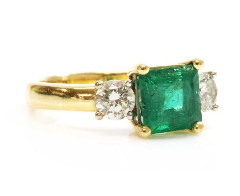 An 18ct two colour gold three stone emerald and diamond ring,with a square emerald cut emerald, four claw set at the cut corn