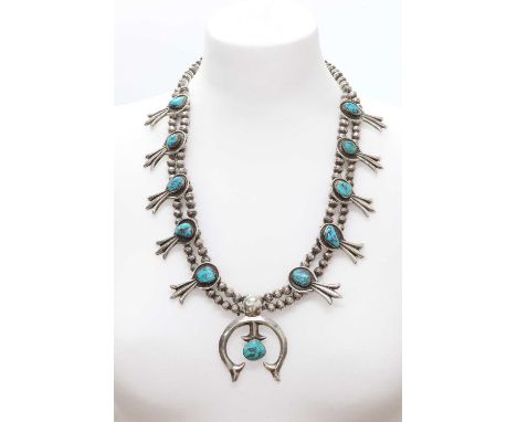 A silver Navajo turquoise squash blossom necklace,with two rows of beads. A chevron section naja with flared ends and a caboc