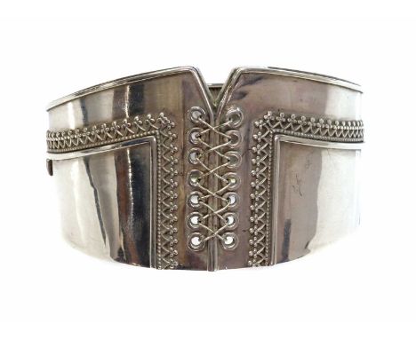 A Victorian sterling silver hinged bangle of corset form,with one straight and one tapered side. A pierced corset style bodic