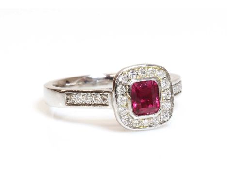 A platinum, ruby and diamond cushion shaped halo cluster ring,with an emerald cut ruby, rub set to the centre. A cushion shap